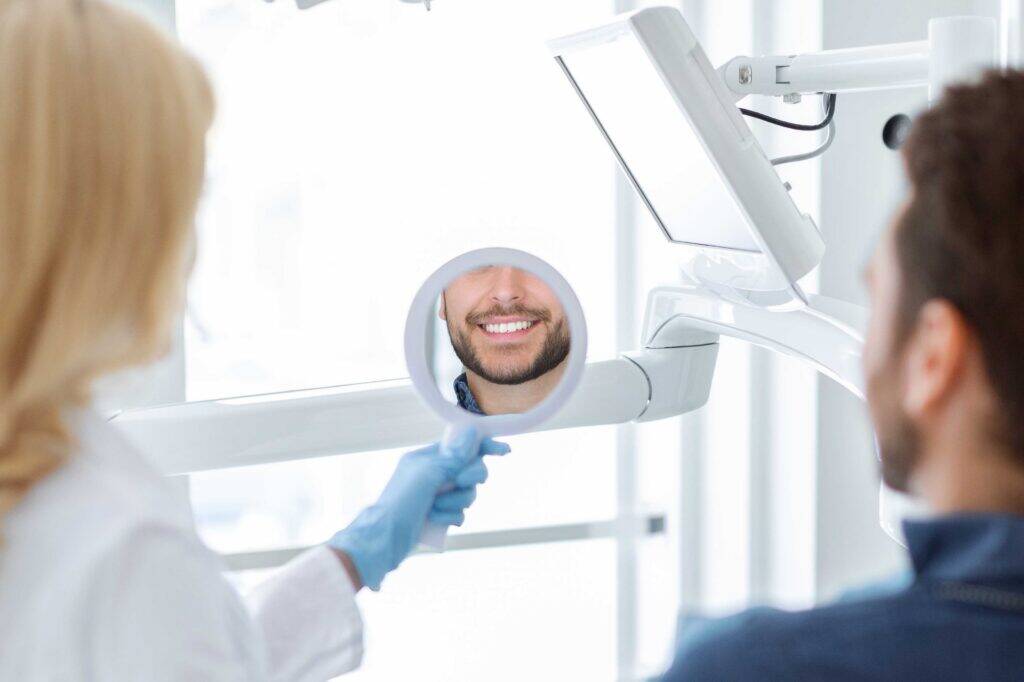 Dentist holding a mirror as a smiling patient looks at their teeth.