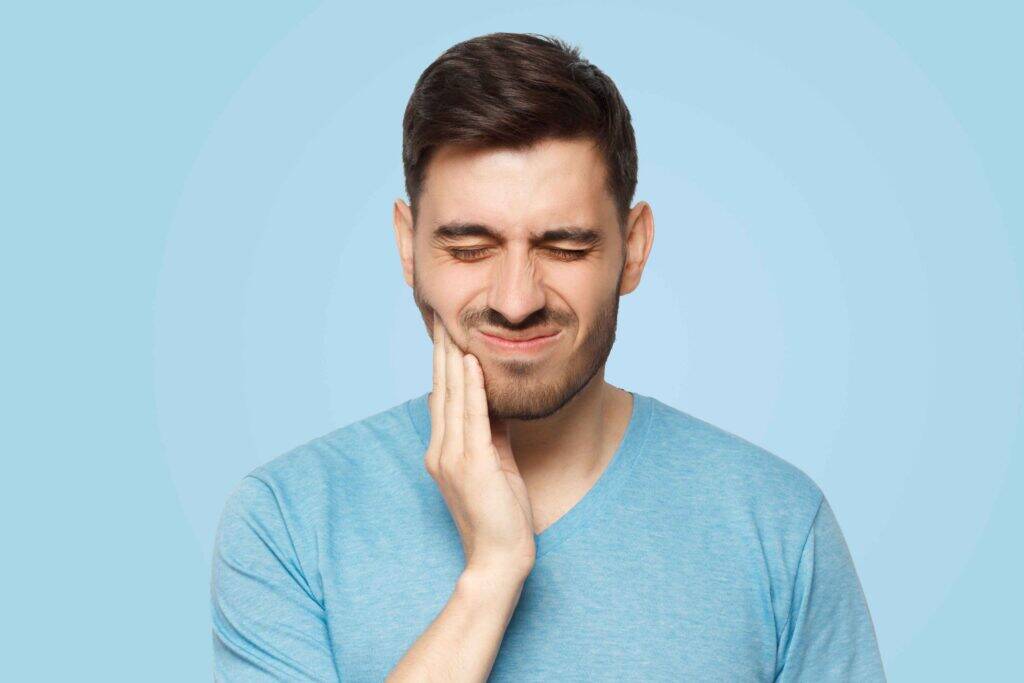 Man holding his cheek while experiencing tooth pain.